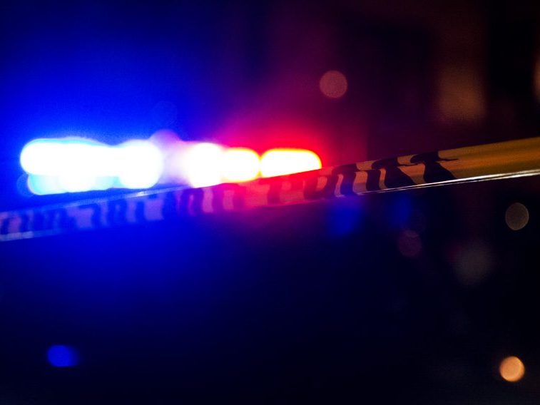 Close-up of police tape with blurred red and blue emergency vehicle lights in the background at night.