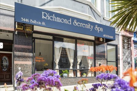 Storefront of Richmond Serenity Spa at 3446 Balboa St., with a blue awning, large front window, curtains, and flowers in the foreground.