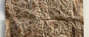 A piece of brown, crumpled paper with an abstract pattern of various geometric shapes and lines covering the surface.