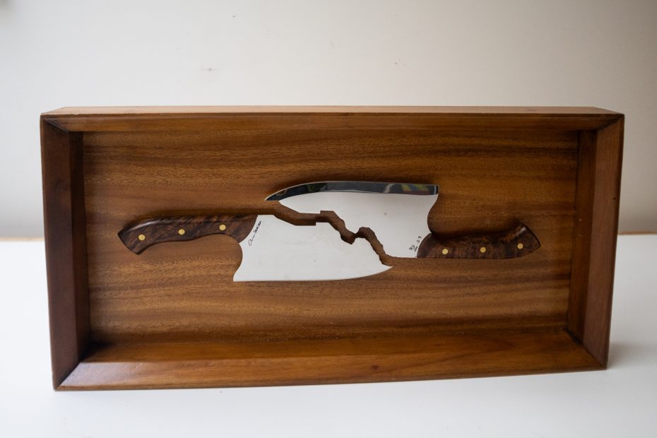 A wooden box displays a large knife split in half, with both halves arranged to align in the center of the box.