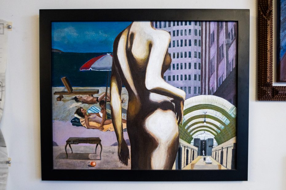 Framed painting of a nude figure in the foreground with a beach scene and buildings in the background, blending surreal and realistic styles.