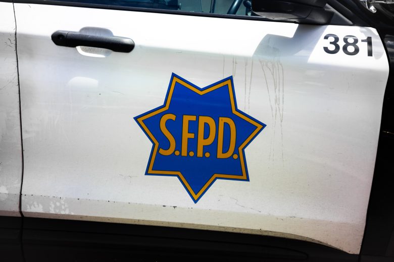 Side view of a white police vehicle with a blue and yellow S.F.P.D. badge logo on the door and the number 381 above.
