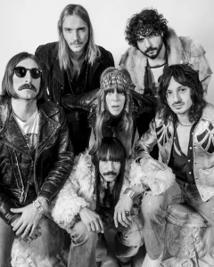 Six people dressed in retro-inspired clothing pose together, facing the camera in a black and white photo.