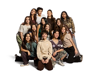 A group of thirteen teenagers pose together against a white background, some standing and some kneeling, all facing the camera.