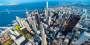 Aerial view of downtown San Francisco with tall skyscrapers, the Bay Bridge, and the bay in the background on a clear day.