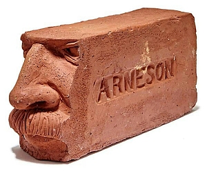 A clay brick sculpted with a human face on one end and the word "ARNESON" engraved on the side.