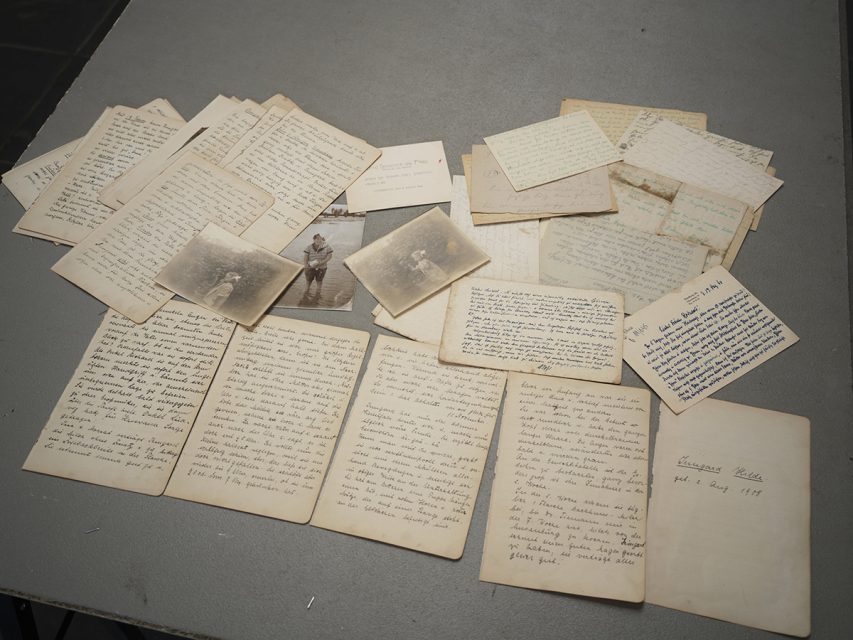 A collection of handwritten letters and old black-and-white photographs spread out on a gray tabletop.