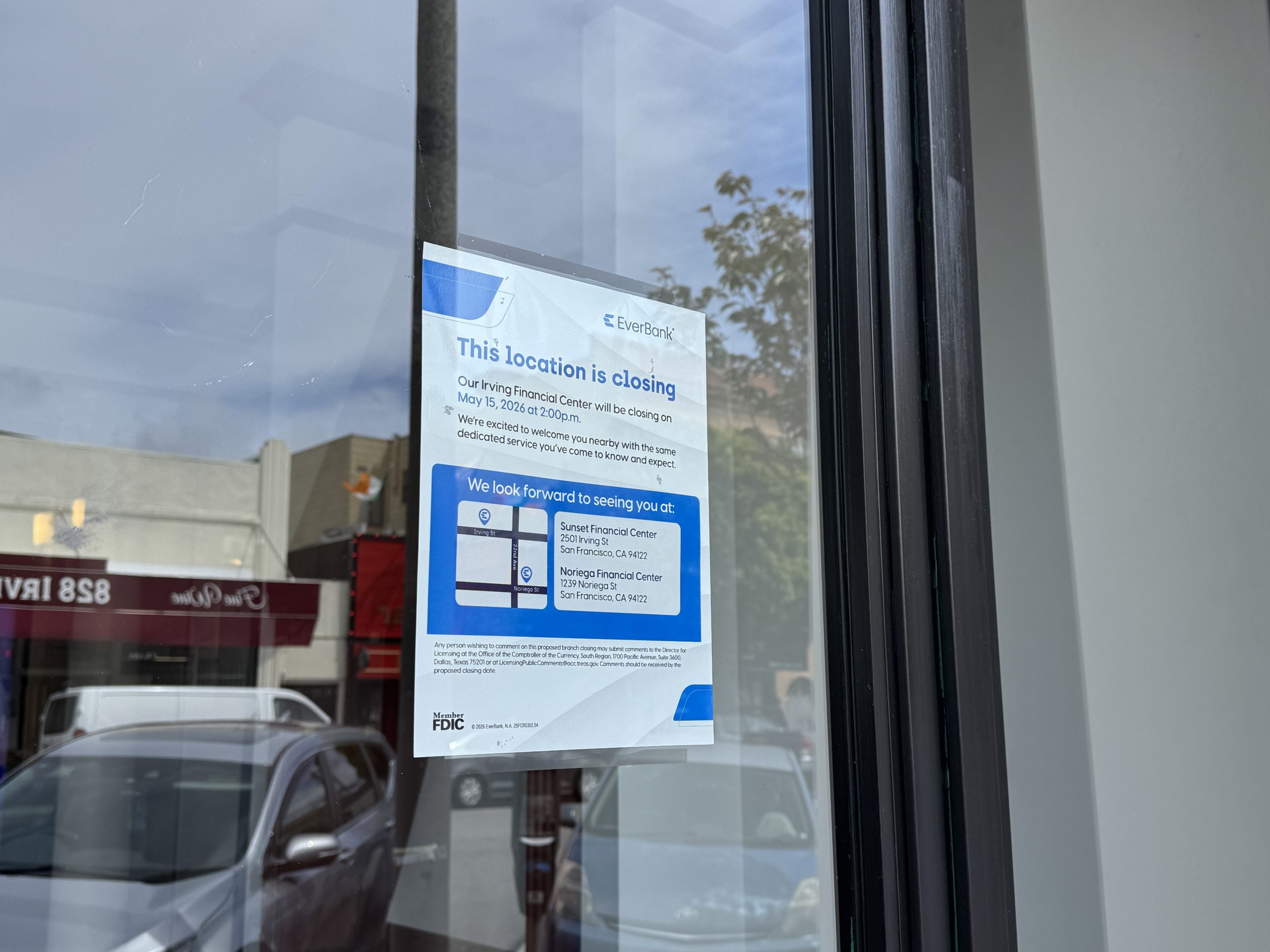 A notice on a glass door announces the closing of an EverBank location, listing alternate branch options and reflecting street and parked cars in the window.