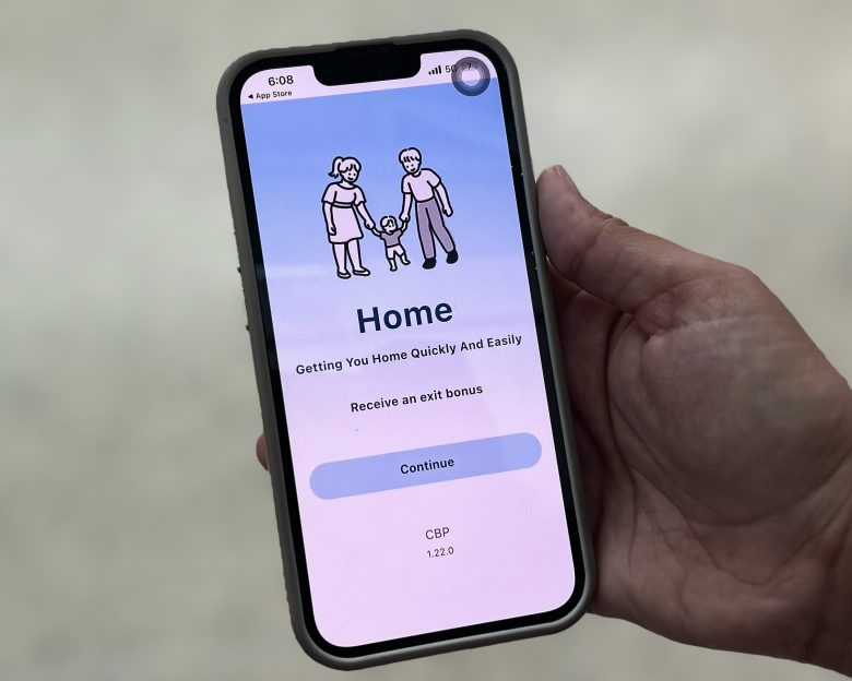 A hand holding a smartphone displaying an app screen with a cartoon family, the word "Home," and a "Continue" button—designed to support every asylum-seeker on their journey to safety.