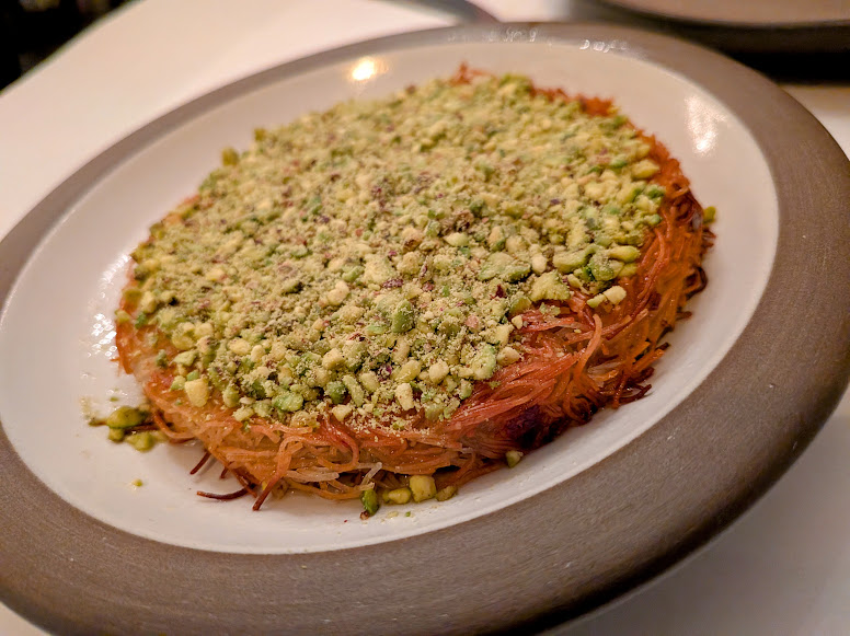 A plate of kunafa topped with finely chopped pistachios, served on a white and gray dish.