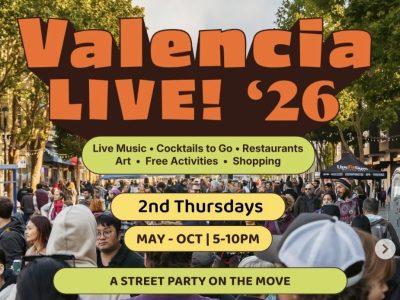 Crowd walking down a city street during Valencia LIVE! '26 event, with banners advertising live music, food, shopping, and monthly Thursday street parties from May to October.