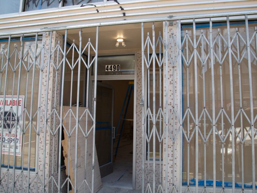 A building with metal security gates, an open glass door showing construction materials inside, and the address number 4490 above the entrance.