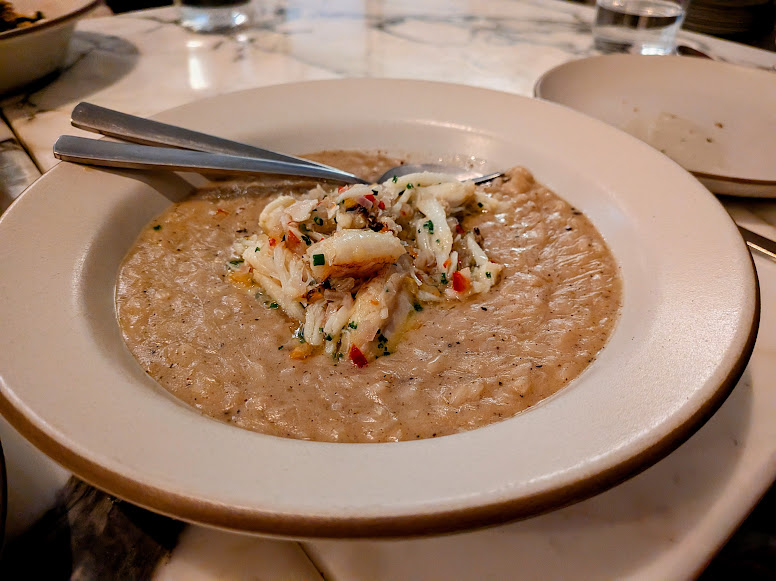 A plate of creamy risotto topped with a portion of crab meat, served with a metal spoon on a marble table.