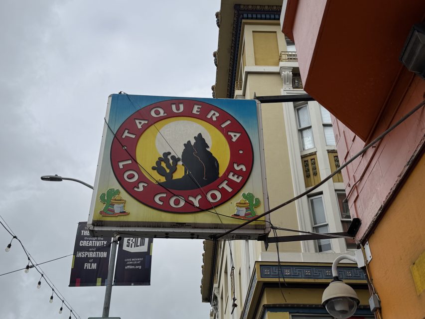 A sign for "Taqueria Los Coyotes" with a coyote silhouette and two cacti, mounted on a building exterior.