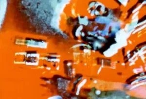Abstract image with bright orange, blue, and white colors, featuring blurred shapes and indistinct objects, creating a sense of motion and distortion.
