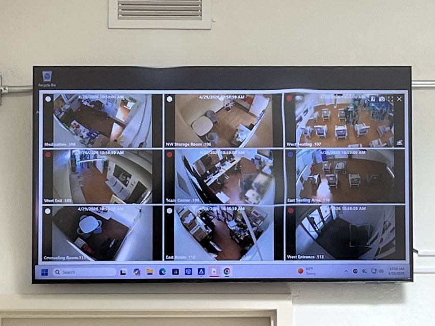 A wall-mounted monitor displays a multi-camera security feed showing live video footage from various rooms and hallways in a building.