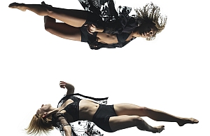 Two women in black dance attire are captured mid-air against a white background, one positioned above the other in dynamic poses.