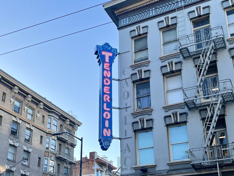 A neon sign reading "The Tenderloin" is attached to the side of the Cadillac Hotel, with fire escapes visible on the building's exterior.