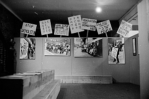 Black-and-white photo of a display with protest signs about housing rights and desegregation, and large photos of demonstrations on the wall.