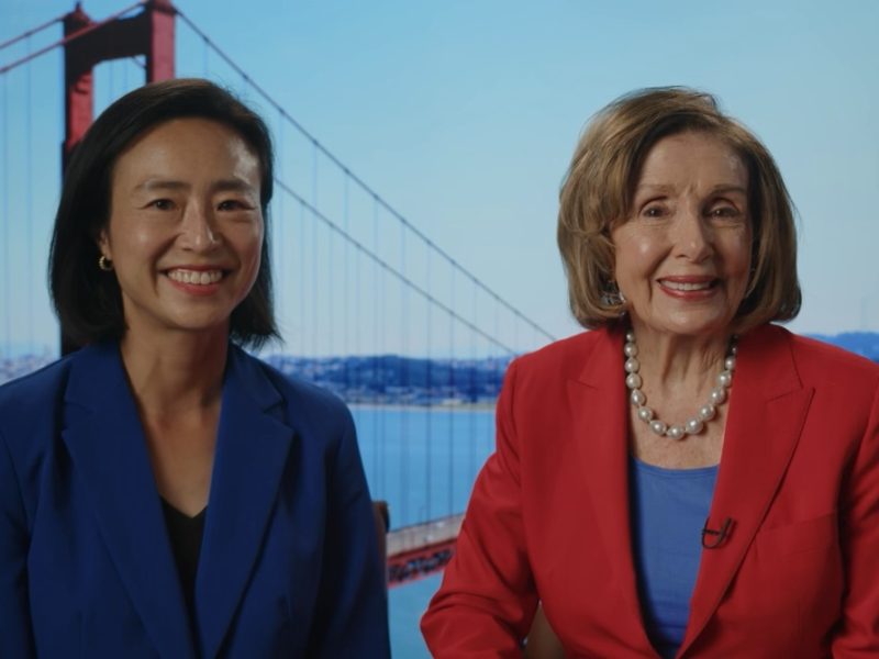Two women in blue and red blazers sit and smile in front of a backdrop featuring the Golden Gate Bridge on a clear day.